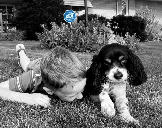 Child lying on the grass with his dog and an ADT sign in the grassp Child lying on the grass with his dog and an ADT sign in the grass