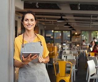 ADT sign on yard A smiling business owner in a yellow shirt and apron stands in a well-lit café, holding a tablet to manage operations.