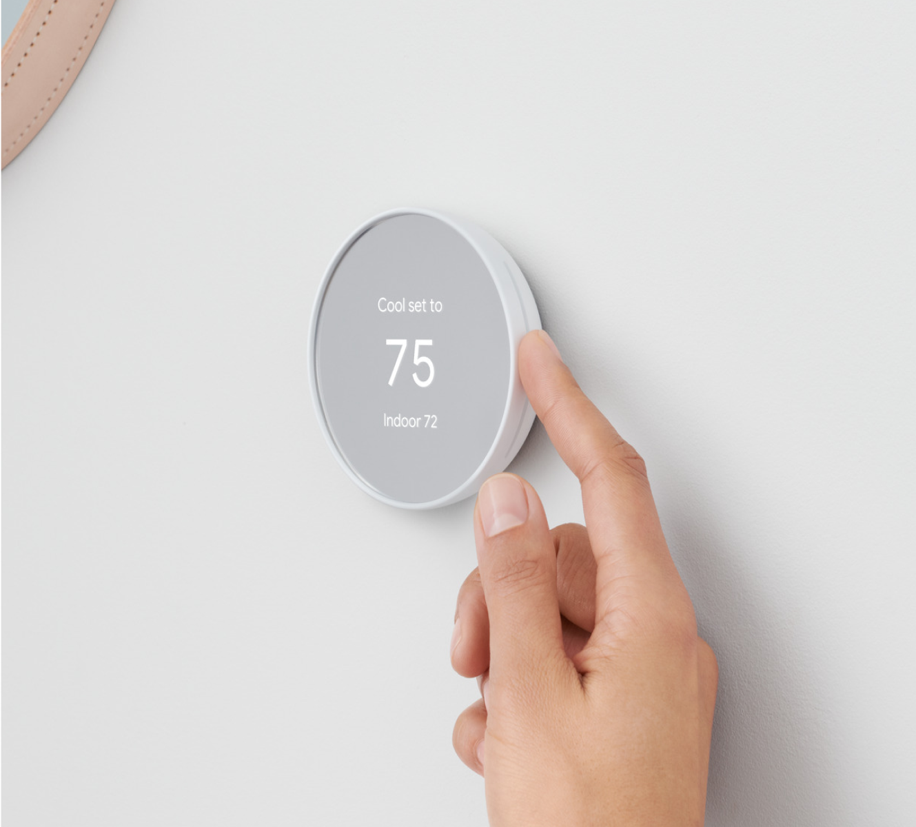 Google Nest Thermostat on a wall with a hand adjusting the temperature Google Nest Thermostat on a wall with a hand adjusting the temperature